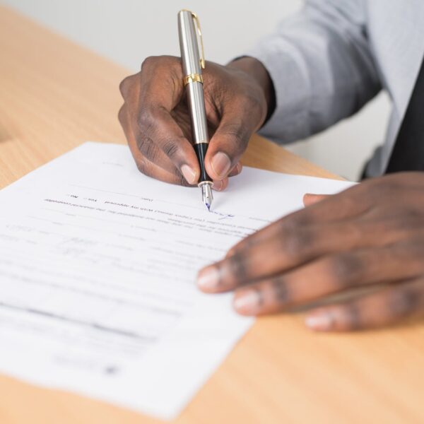 person holding gray twist pen and white printer paper on brown wooden table